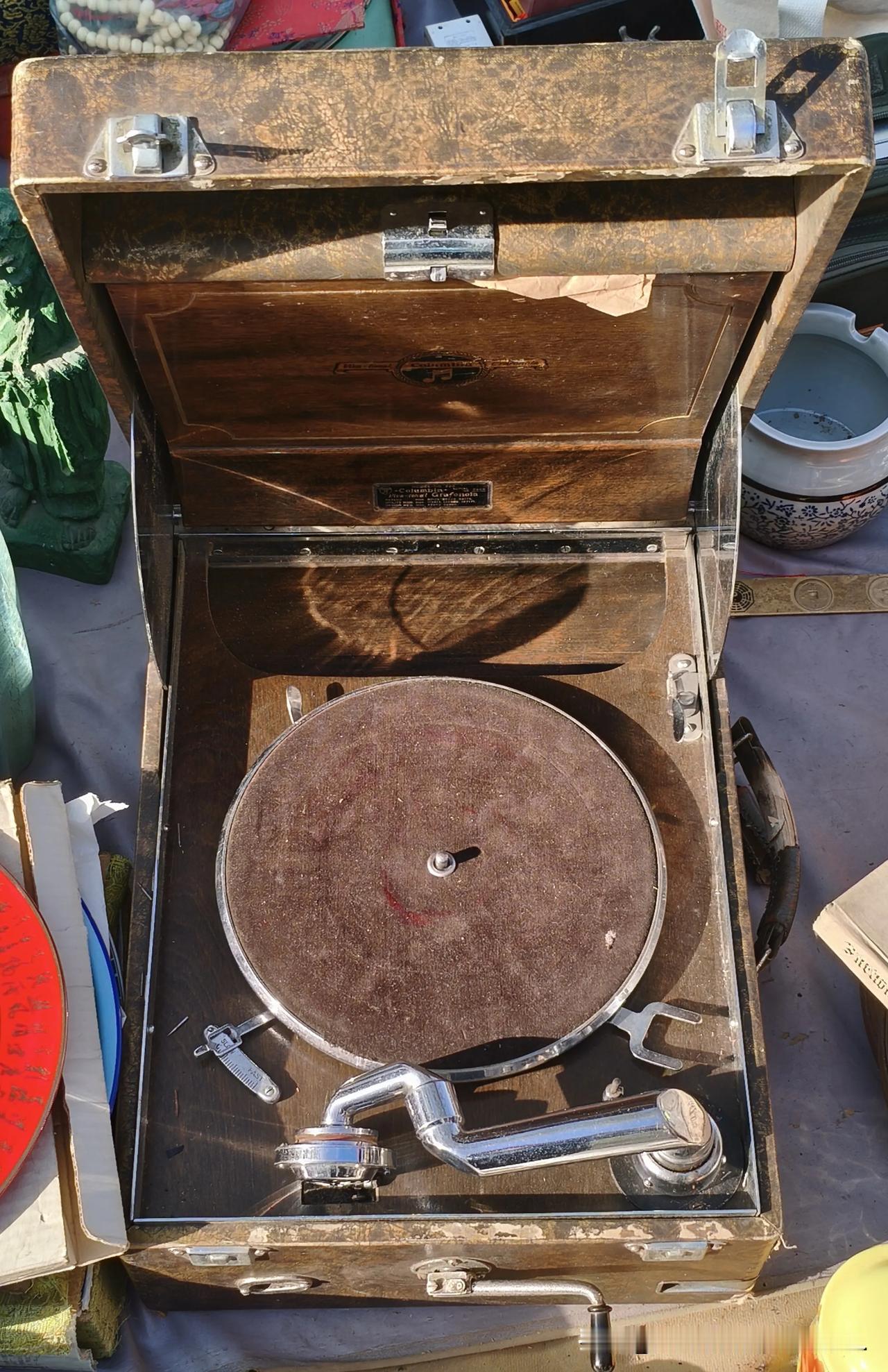 旧货摊的晨光里，这台老留声机静静躺着。木质箱体刻满岁月痕迹，唱臂仍保持着等待的姿