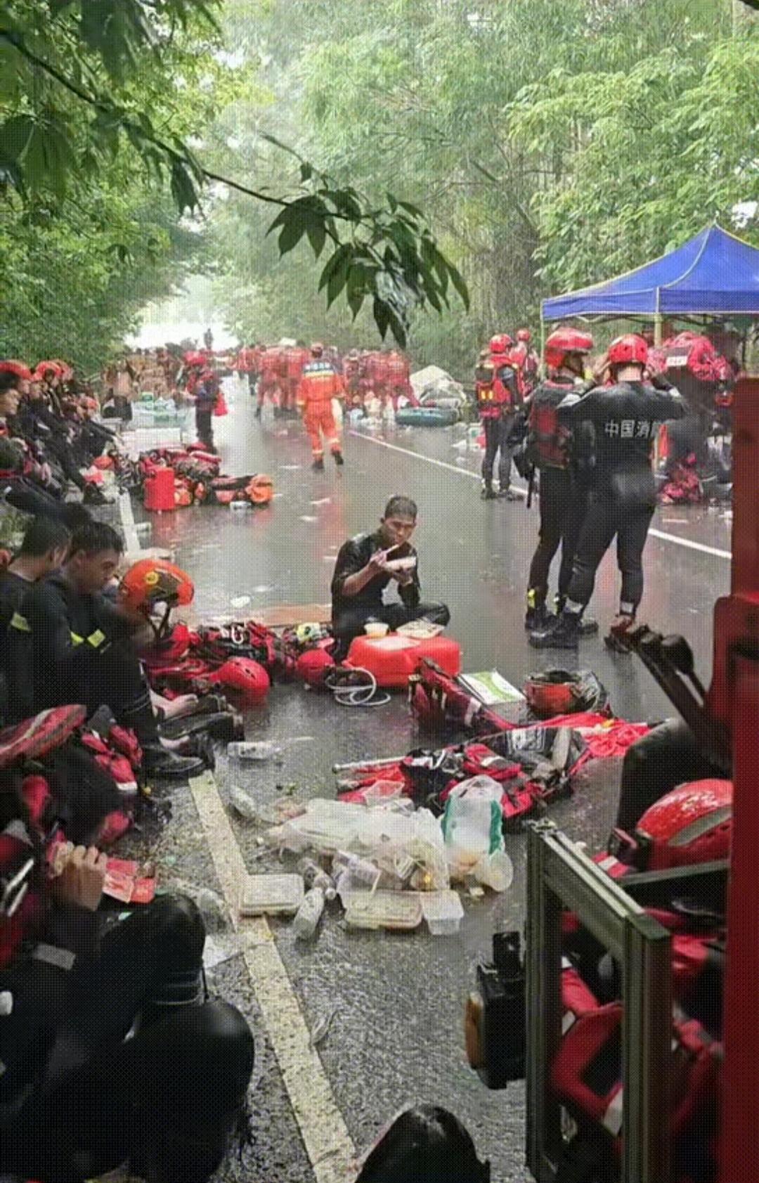 消防战士盘腿坐在地上吃饭，老天爷偏在这个时候又开始肆虐，雨又哗啦啦地下了起来。豆