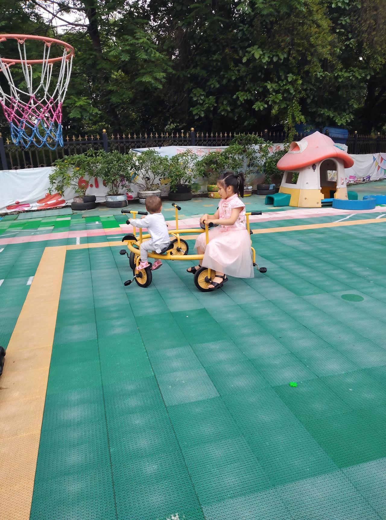 阳光暖暖的，幼儿园的操场上格外热闹。姐姐穿着漂亮的粉色裙子，带着小小的弟弟一起骑