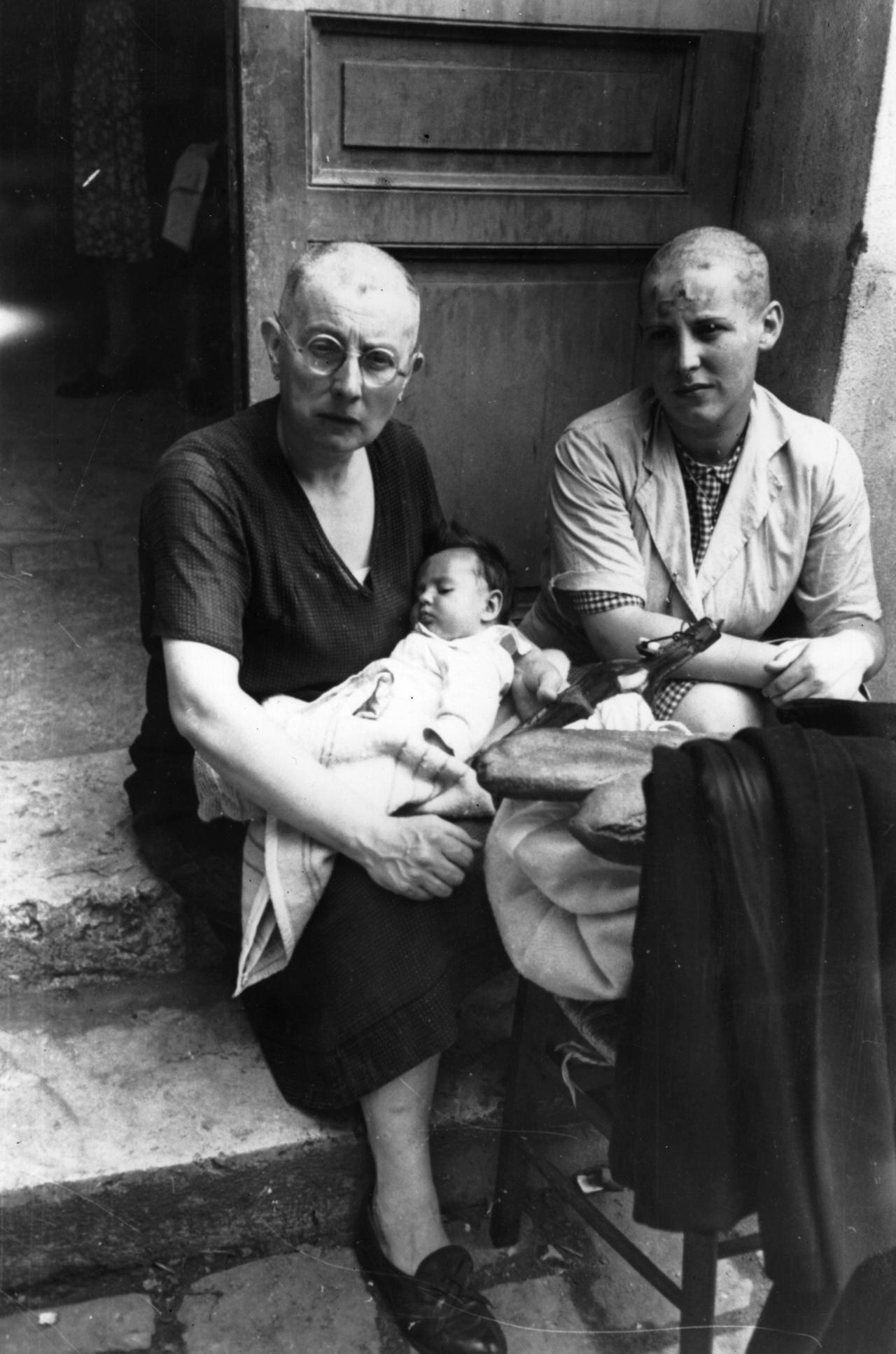 1944年。两名剃着光头的法国妇女，一对母女，她们与德国人保持着联系，坐在房子门