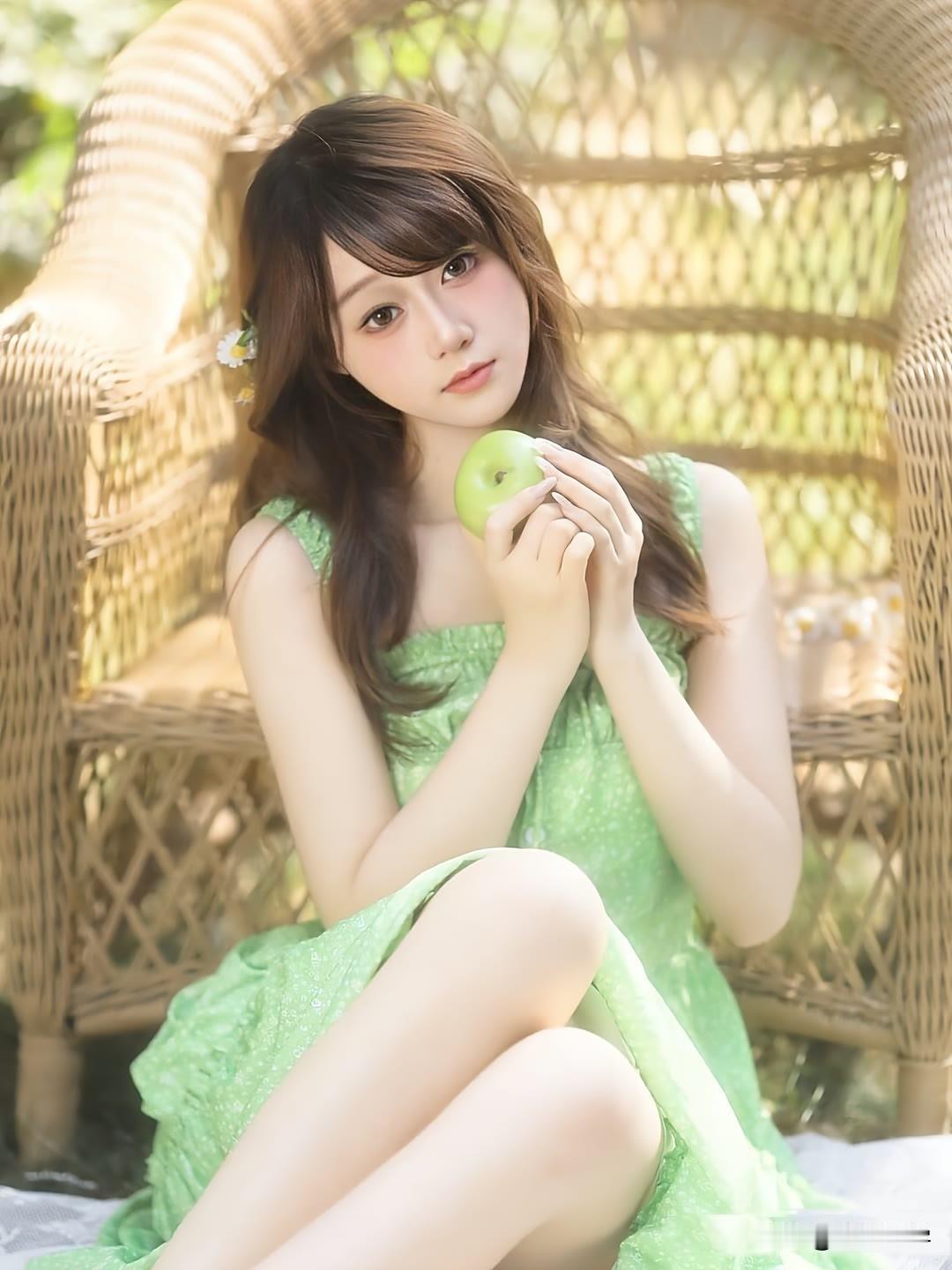 女孩坐在藤椅上，拿着一个苹果。苹果少女照
