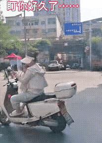 马路上有辆摩托车晃得有点厉害，前面站着个小孩，后边的妈妈一手扶车把，一手拿着手机
