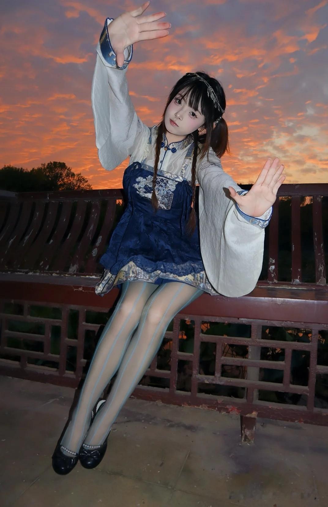 这位姑娘穿着古装，坐在栏杆上，背景是美丽的晚霞。
