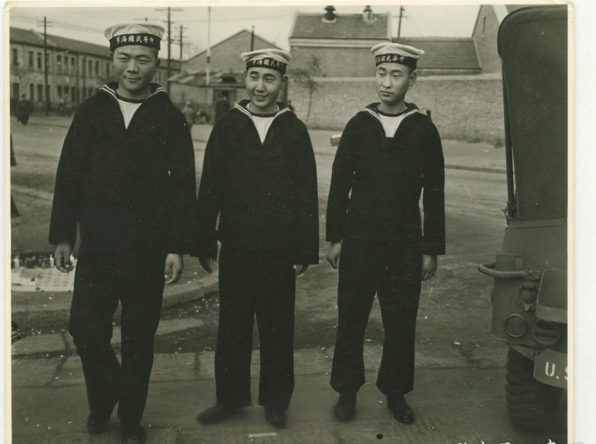 1945年的青岛，海风裹挟着历史的余韵掠过街道。三位民国海军军人立于砖石路面上，