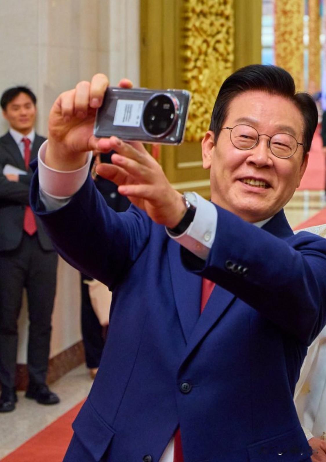 李在明拿小米Ultra 15手机拍照。这是APEC时，李在明收到的中国国礼。访华