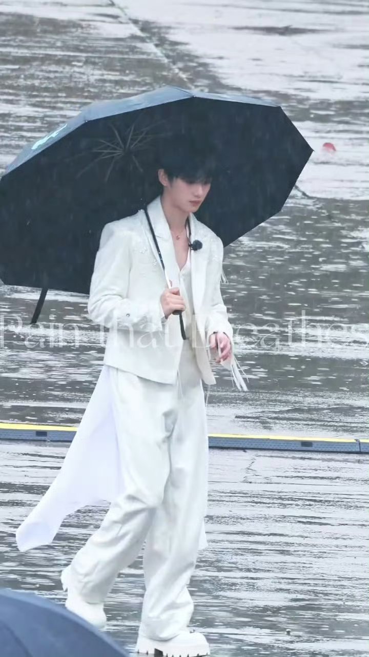 丁程鑫录制时遇雨，一身白色西装撑着伞，边走边和粉丝打招呼，那模样像极了来接公主的