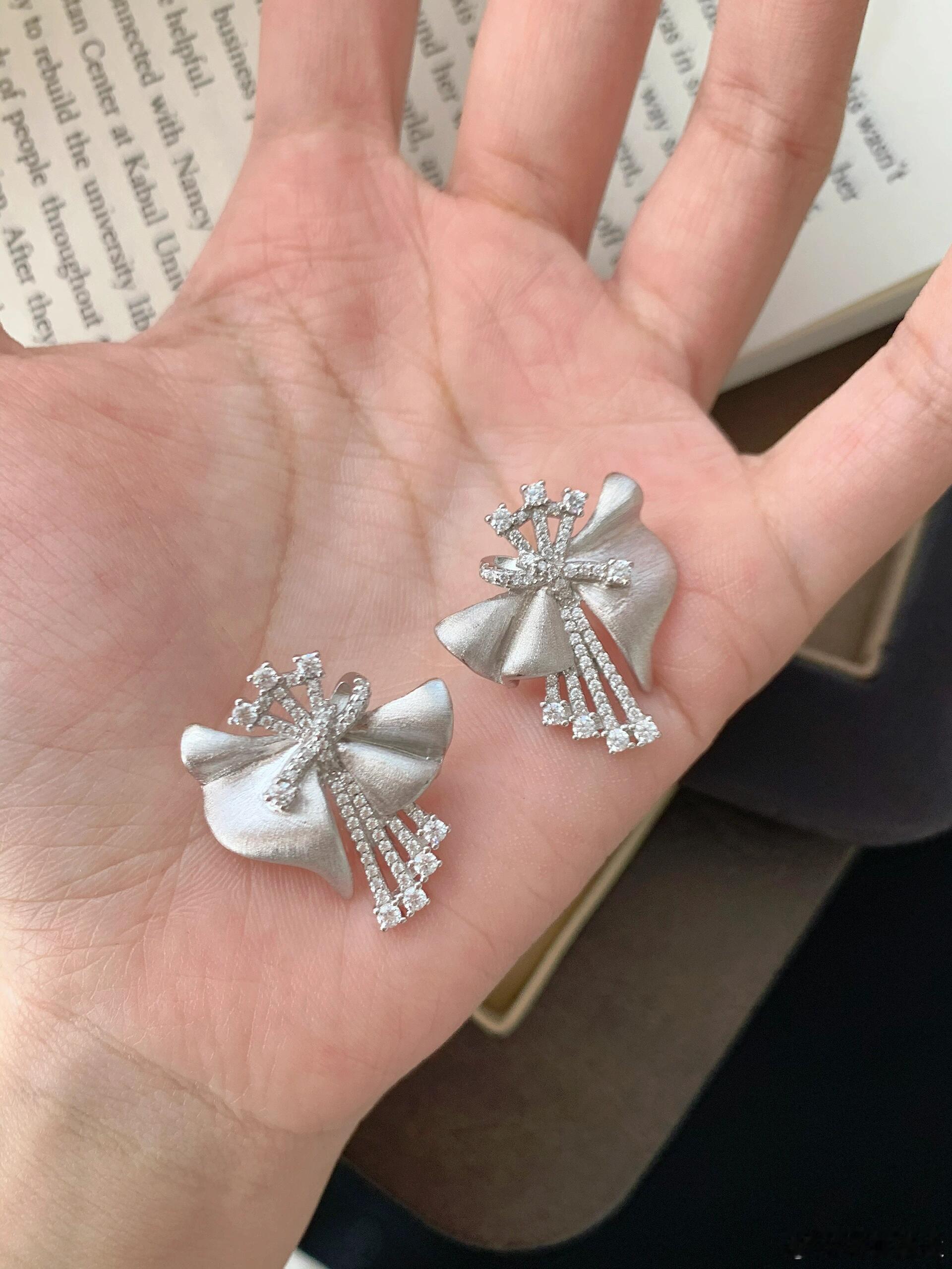 这款耳钉以精致的立体蝴蝶结造型呈现，通体镶嵌闪耀水晶，在光线折射下璀璨夺目。银色