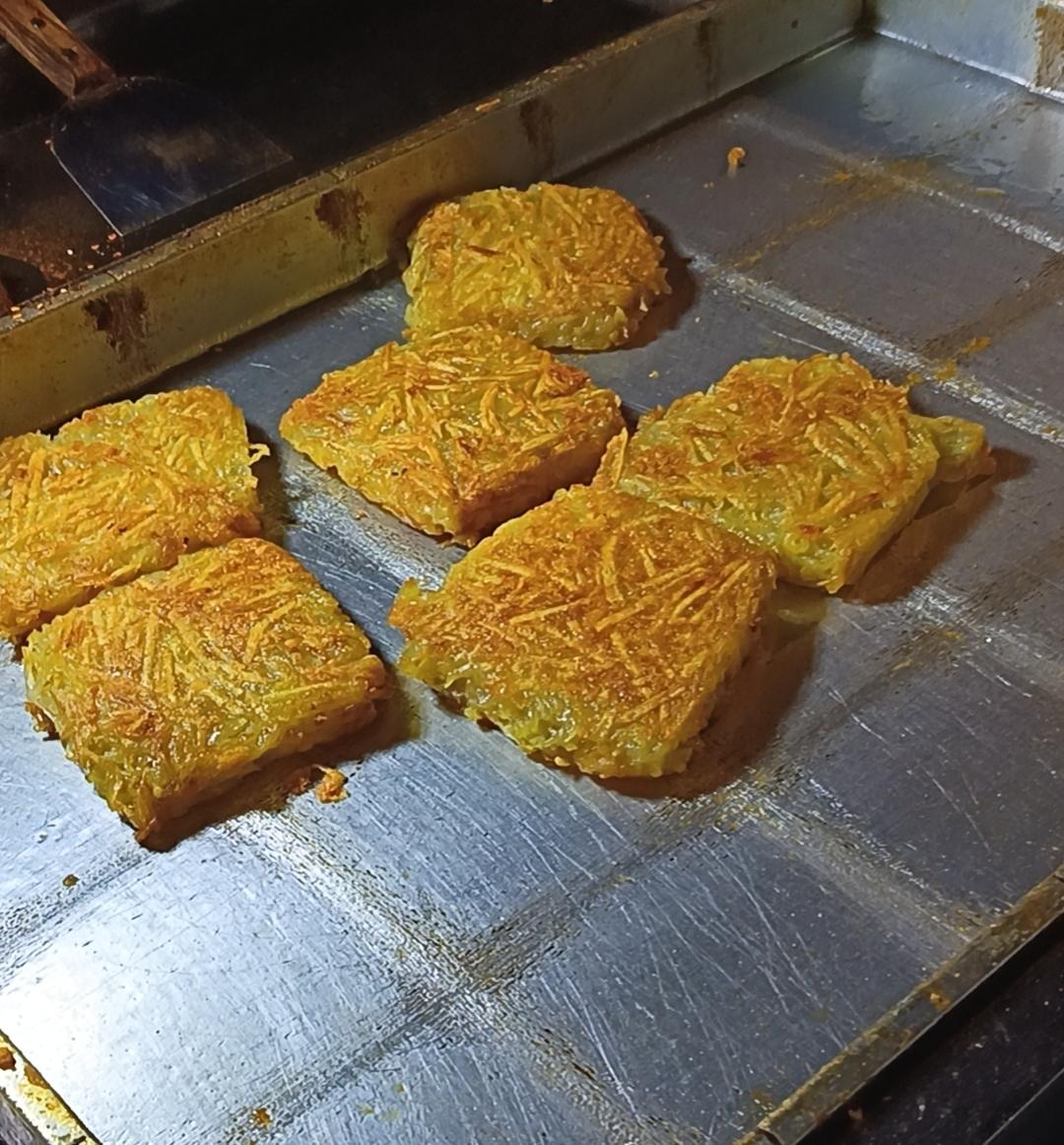 昨晚逛夜市，刚走到小吃摊前就被铁板上的洋芋粑勾住了脚步。金黄的洋芋丝压成方块，在