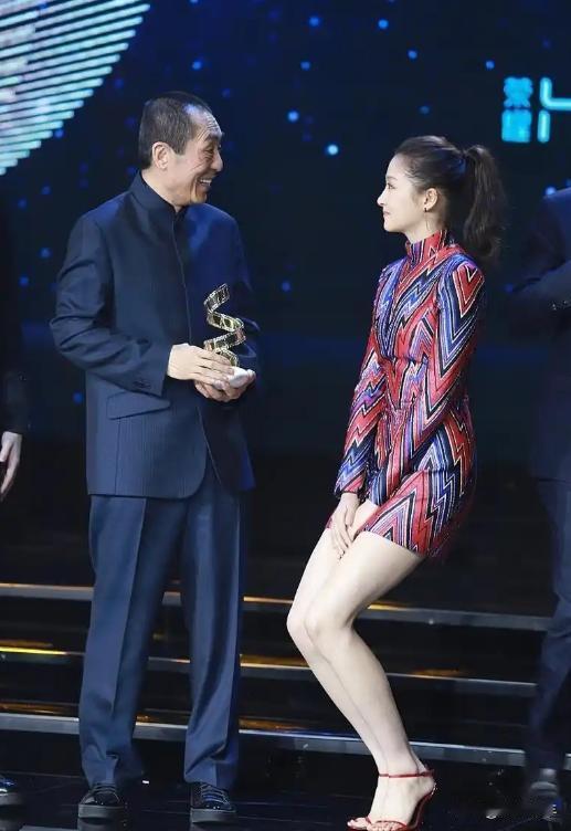 她在电影界颁奖盛典上，面对张艺谋递来的奖杯，为防宽大礼服裙摆扬起不雅并表达对前辈