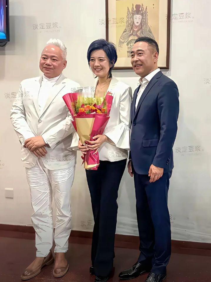 中间美女的笑容很迷人，看着就特别亲切。一身白西装搭配黑裤子，手里捧着鲜花，整个人