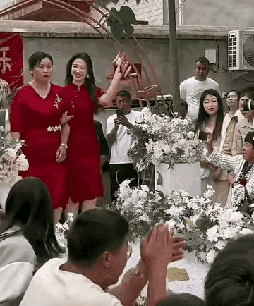 这两位女士，穿着大红喜庆的旗袍，一位喜气洋洋，一位愁容满面的，不知哪位是喜婆婆，