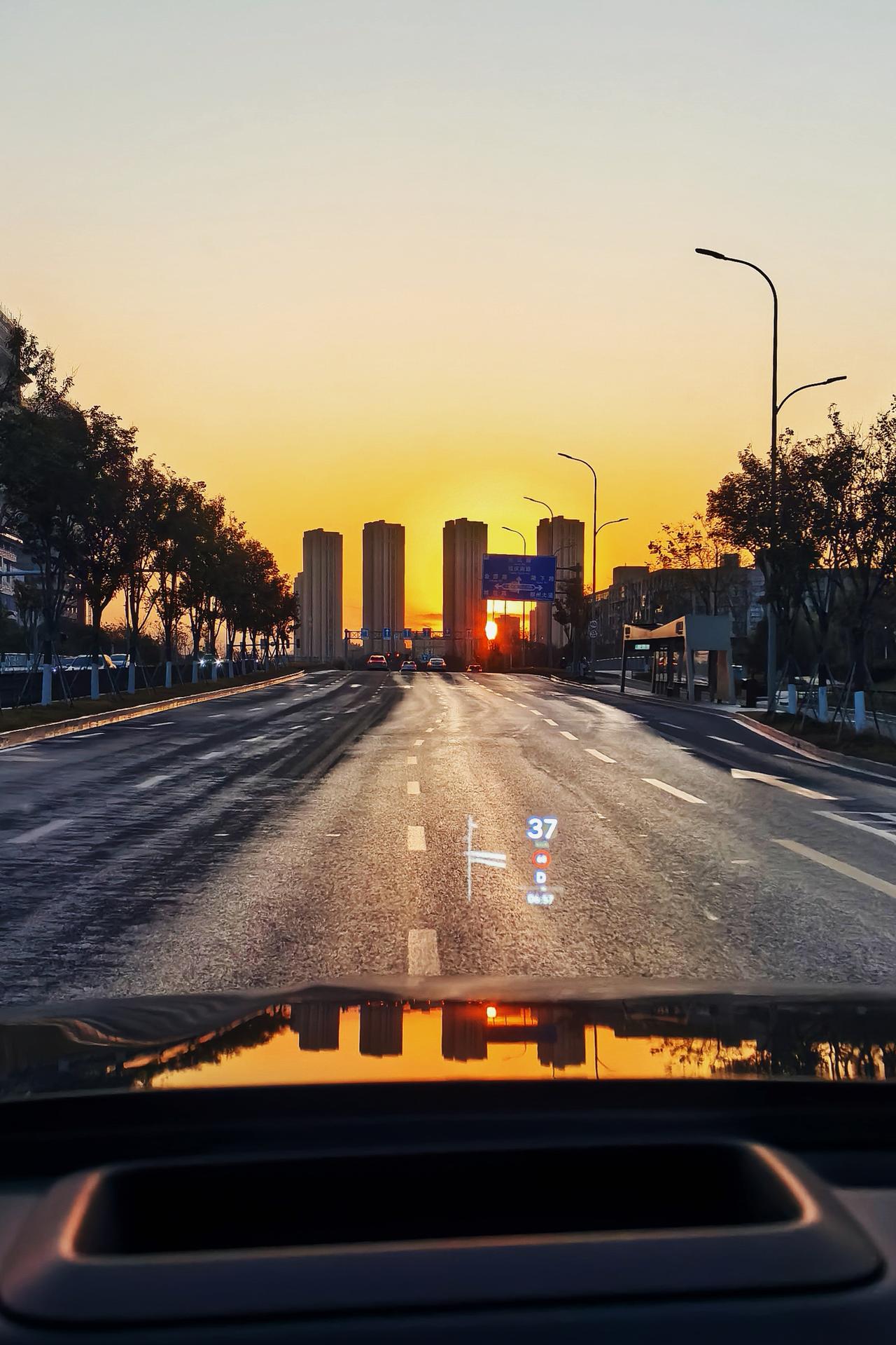 千问配文：晨光破晓，城市苏醒。车行于宽阔大道，前方高楼剪影与朝阳相映成辉，路面微