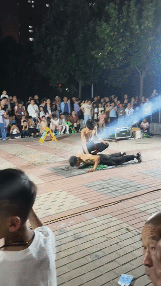 两名身材瘦弱的男子在街头卖艺。
光着膀子在碎啤酒瓶玻璃渣上滚来滚去？
看起来真是