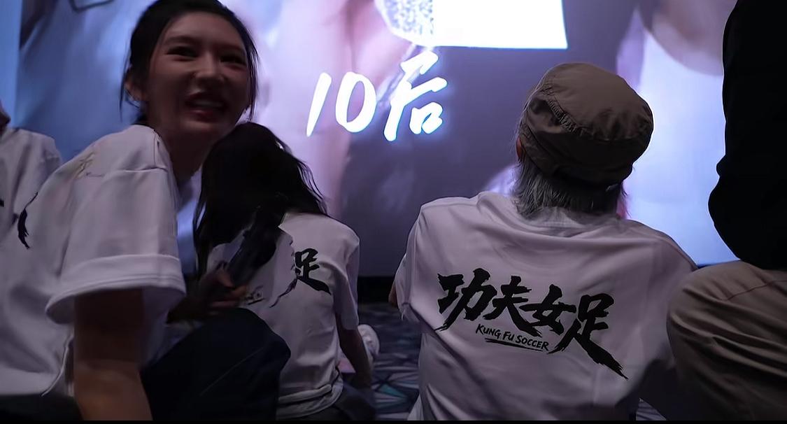 周星驰坐在地上看着全国各地对《功夫女足》的声援，有包场拉横幅的、有出租车打广告的