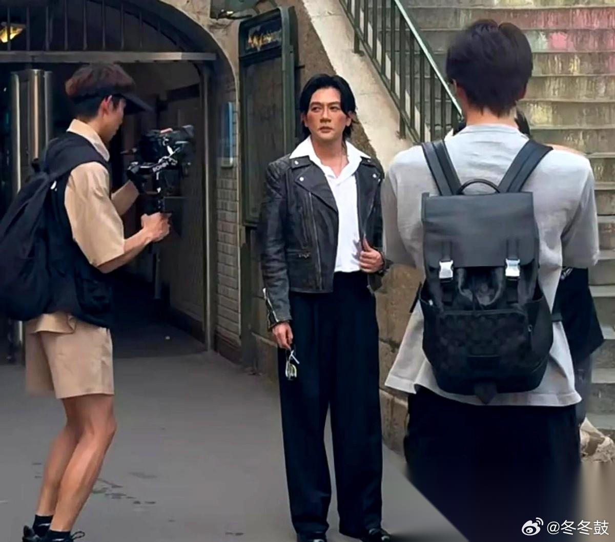 巴黎街头32度的高温下，一群穿着短袖短裤、猛摇扇子的工作人员中间，杵着一个裹着厚