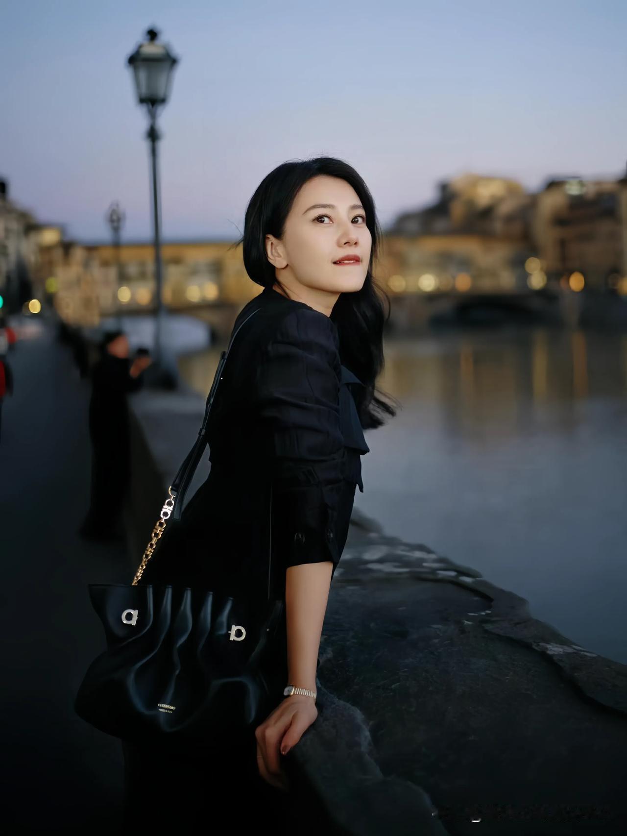 漫步在异国街头，高圆圆于河畔、古墙旁留下倩影。一身简约黑衣，搭配精致黑包与玛丽珍