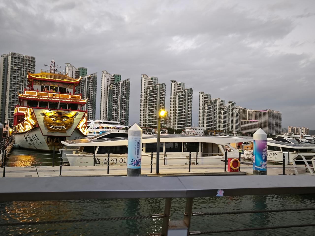 分享一张相册里随手拍的天空阴云笼罩的三亚码头，中式仿古游船的鎏金灯火撞进冷调的城
