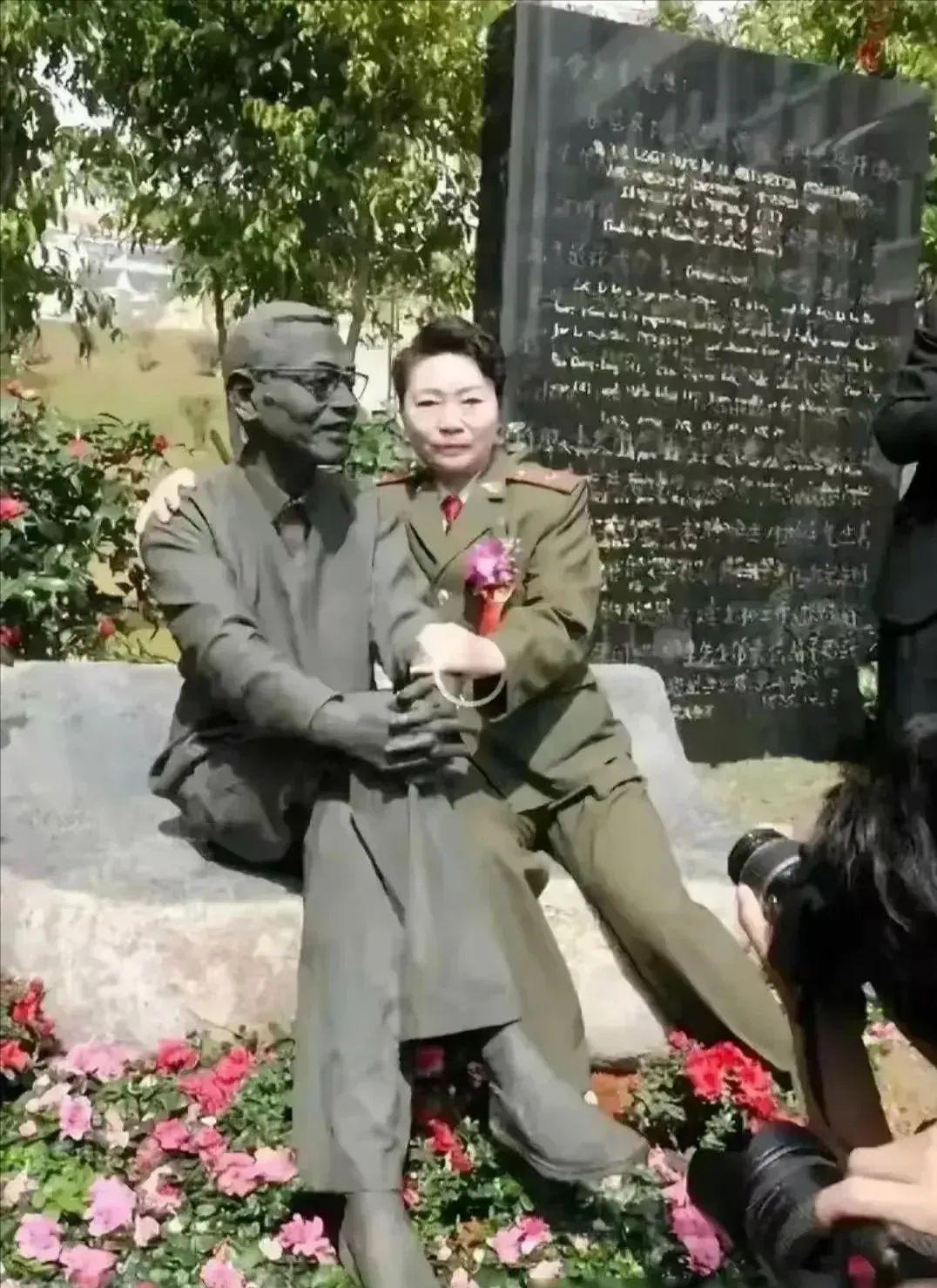 由昆坐在丈夫陈景润的铜像旁，她一只手揽住“丈夫”的肩膀，另一只手挽着他的胳膊，饱