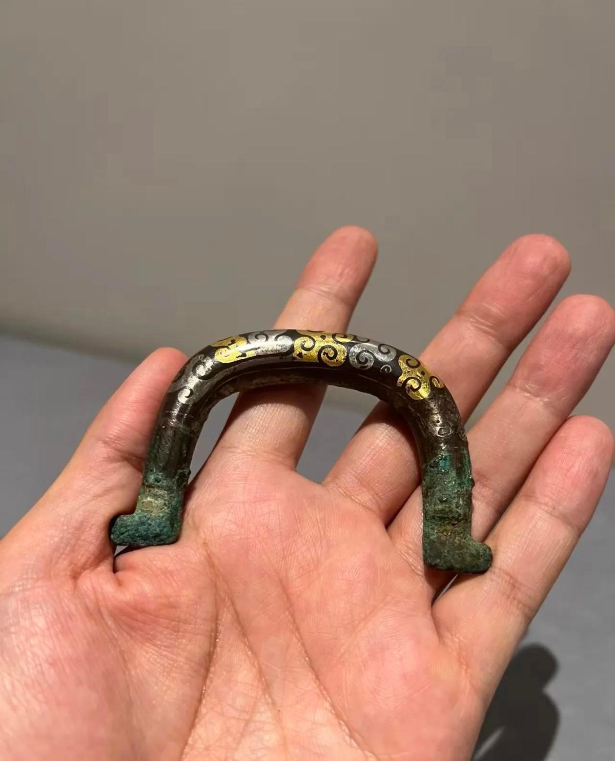 邻居在河边洗竹筐时捞上来个把手，放在手掌心里大小正好，上面刻满了花纹。U形的青铜