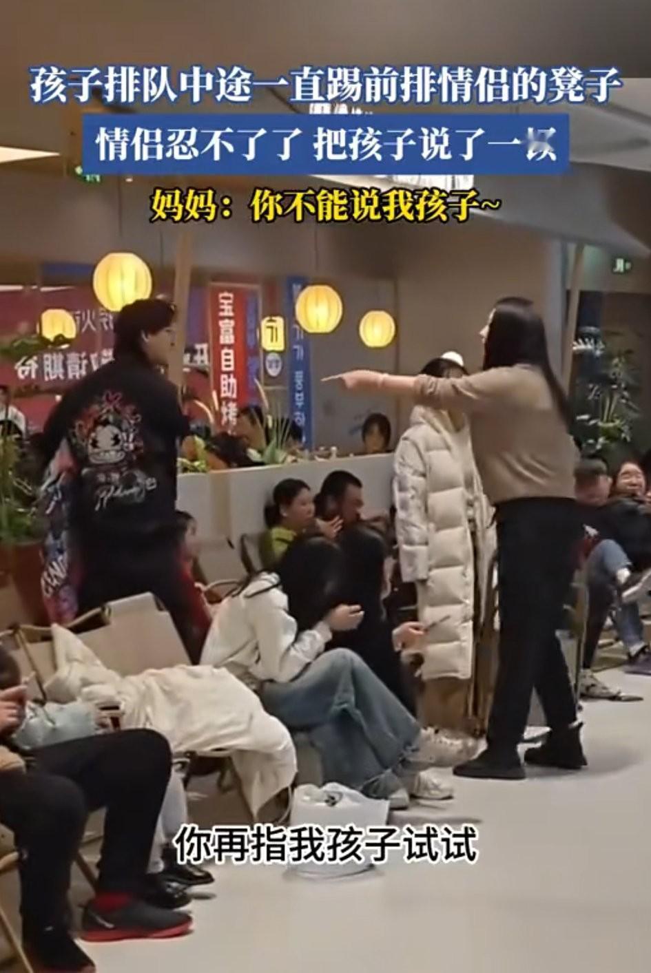 商场内，两排椅子上坐满了人都在排队，情侣坐在前面，母子坐在后面 ，孩子踹前面的椅