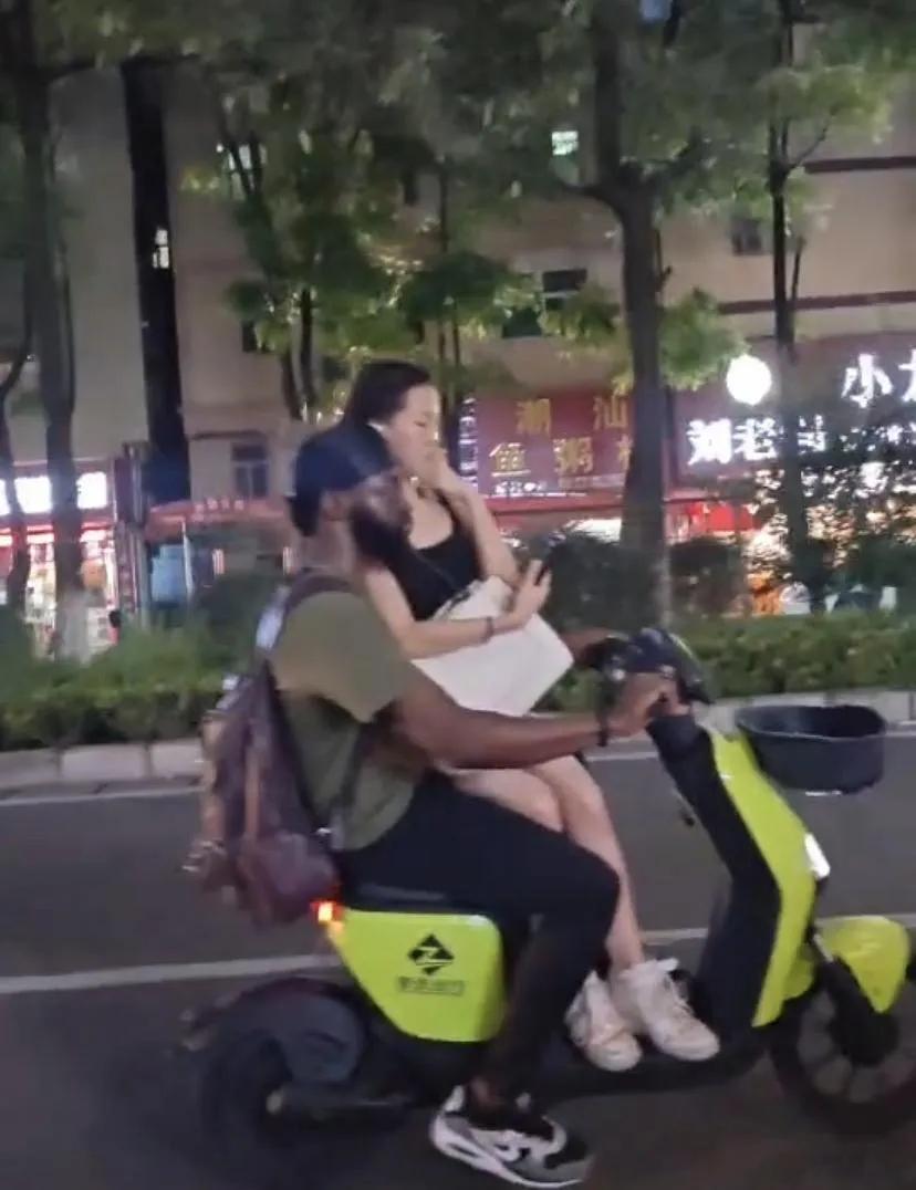 她居然还会不好意思？一非洲男子骑电动车载个东大女生，路人拿手机拍，女生立马用手遮
