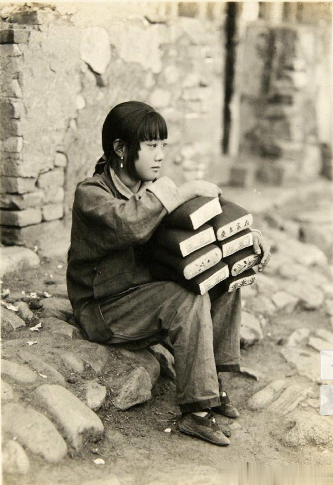 1926年，外国摄影师在北京城郊一条巷子里拍摄的一个卖枕头的小女孩。她静静地坐在