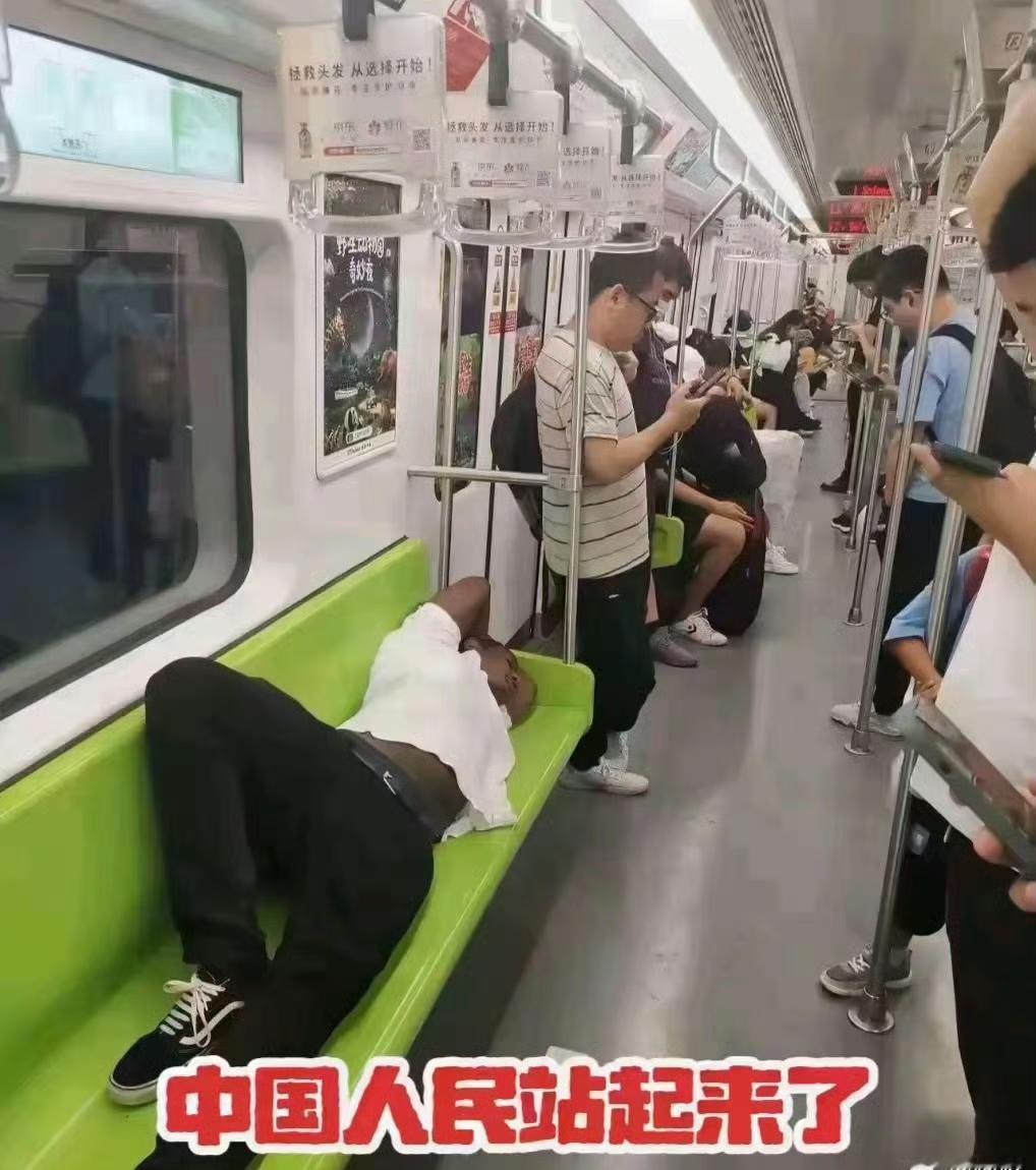 一个黑人小伙一人躺平一条座椅，怡然自得，这是哪个城市哪条地铁。周围的小伙默默地玩