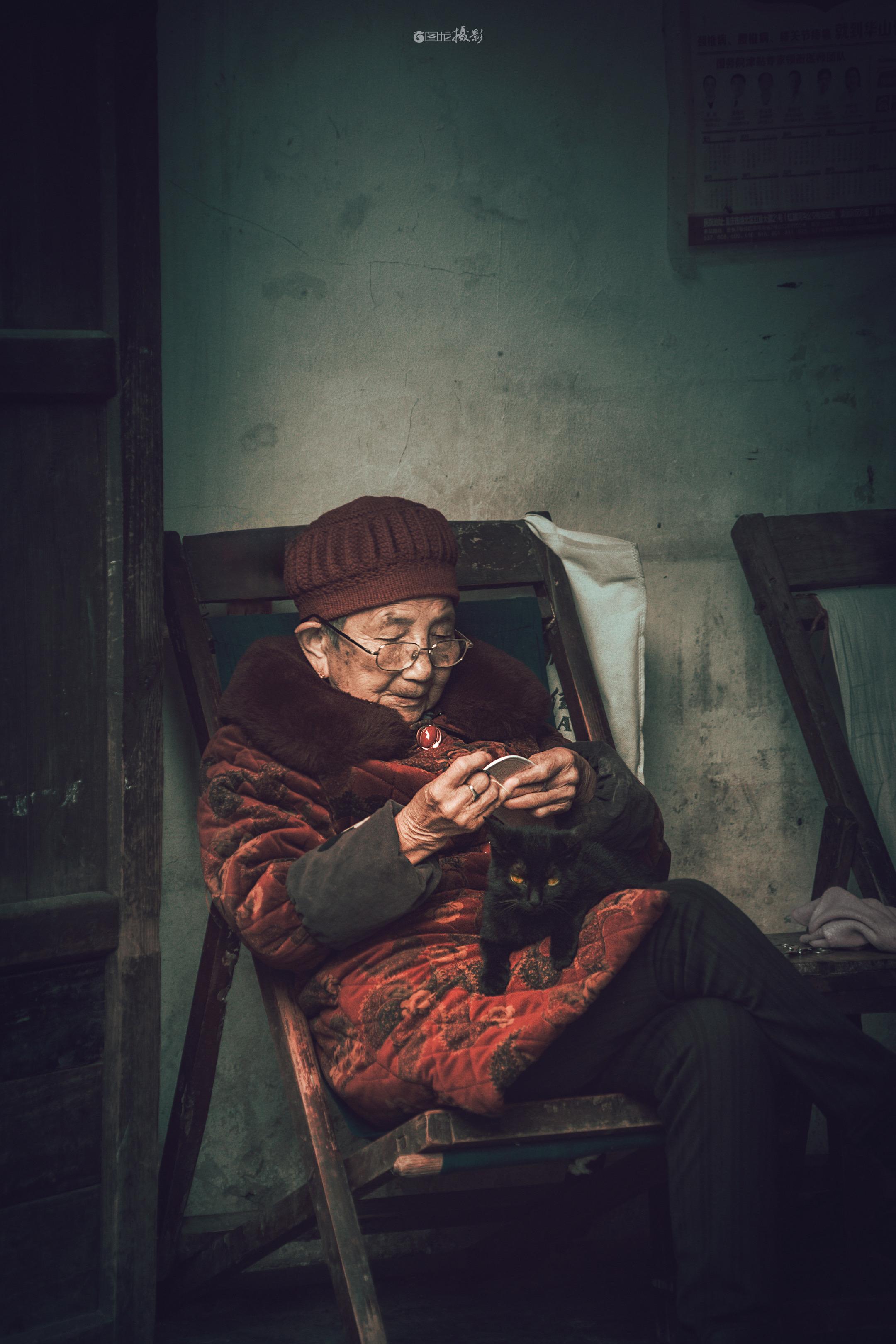 时光慢叙。在斑驳的老墙下，时光仿佛被调成了慢镜头。老人裹着红棕的棉服...