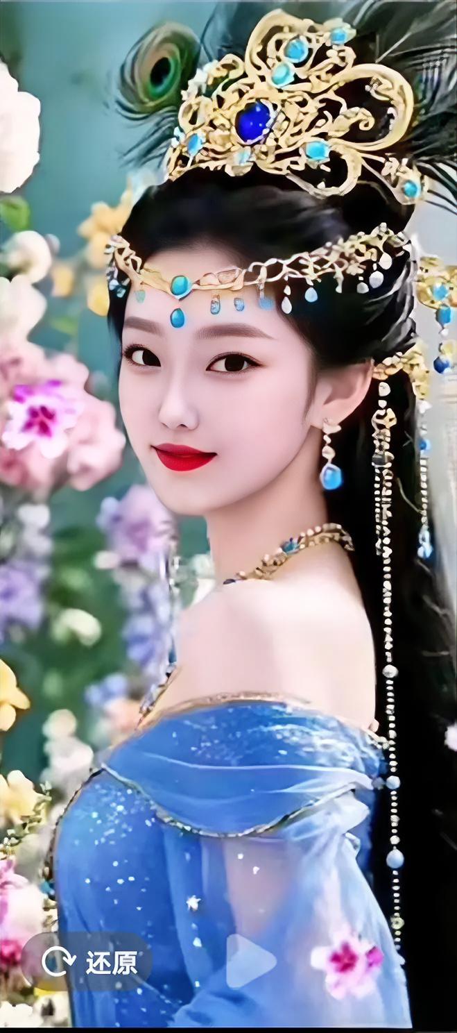 一袭冰蓝纱裙缀满星光，鎏金头饰嵌着澄澈宝石，额间坠饰轻垂，乌发间羽饰翩然，眉眼温