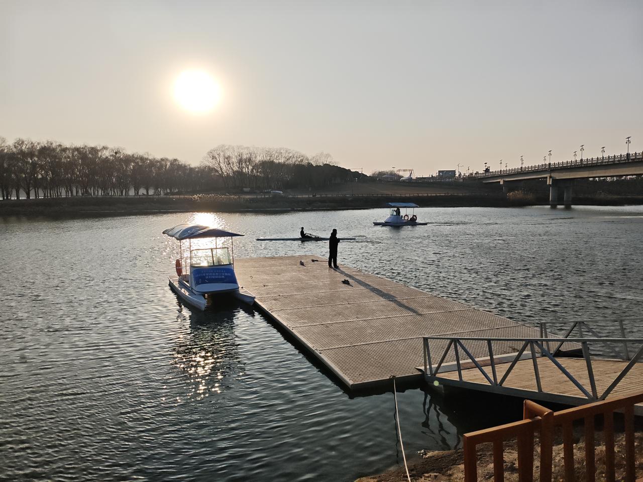 冬日生活打卡季落日把河面揉成碎金，采风的脚步停在浮桥边。波光里泊着脚踏船，一人立