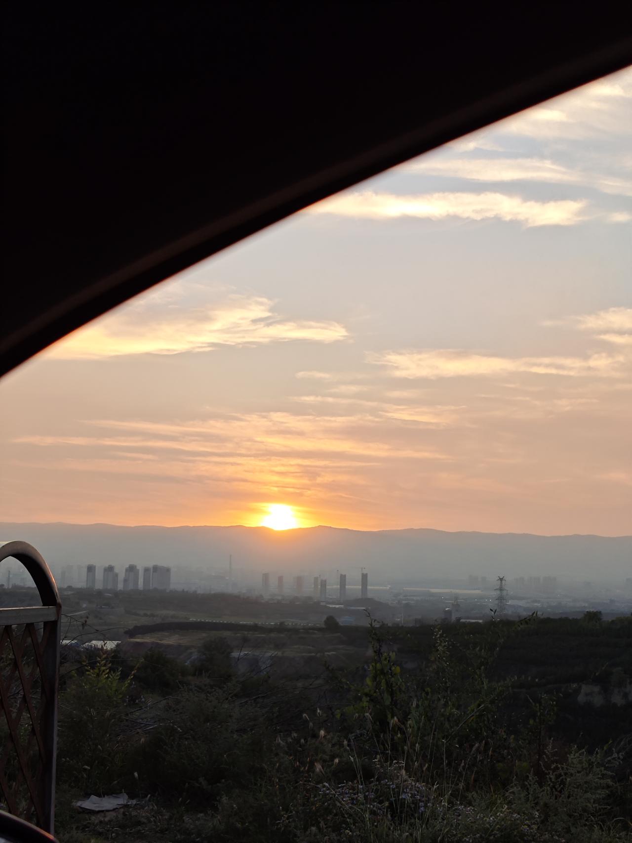 我拍到的落日瞬间夕阳西下，远处的高楼在落日余晖中朦朦胧胧，我把车停在路边，用手机