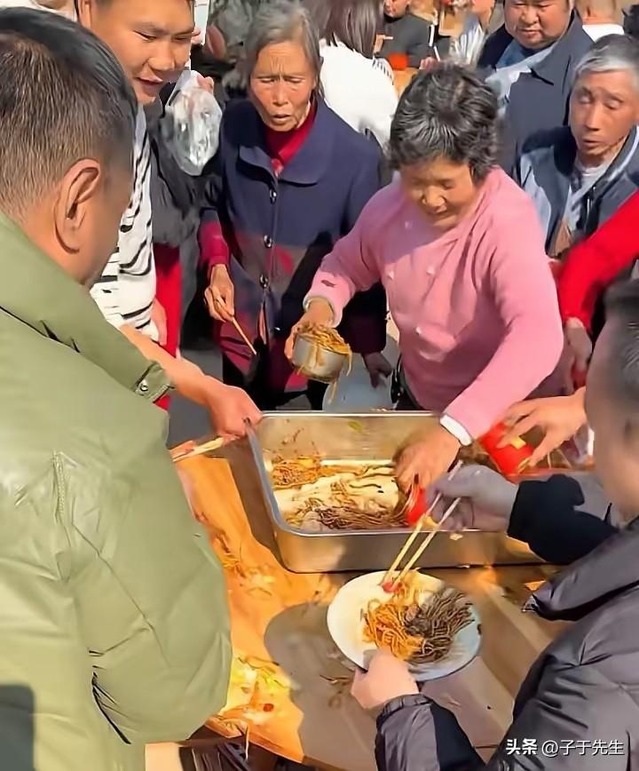 江西丰城的杀猪宴现场呈现出一种无序喧闹的景象，仿佛旧时灾荒年间赈济场面重现，人群