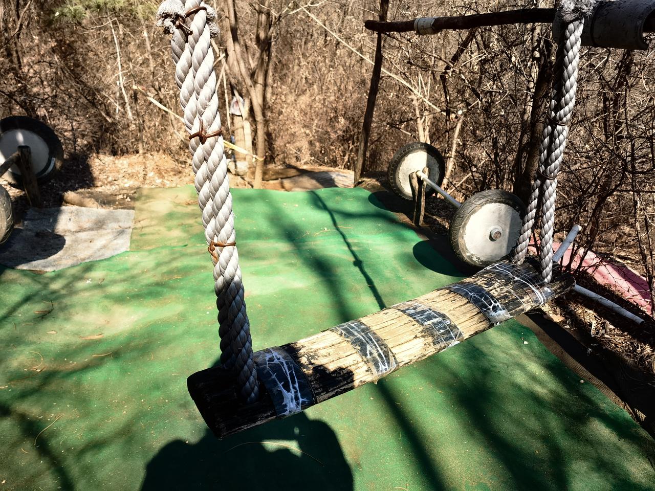 山上一角，有一小块儿练功场，那儿有一个秋千。
秋千用木条拼出来的。灰褐色的木条，