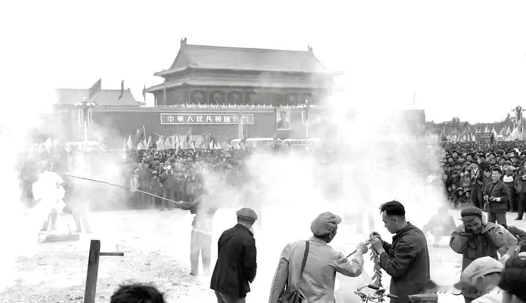 六十年代的天安门广场，人群密密麻麻汇聚于此，人们忙着燃放鞭炮，白烟滚滚弥漫开来，