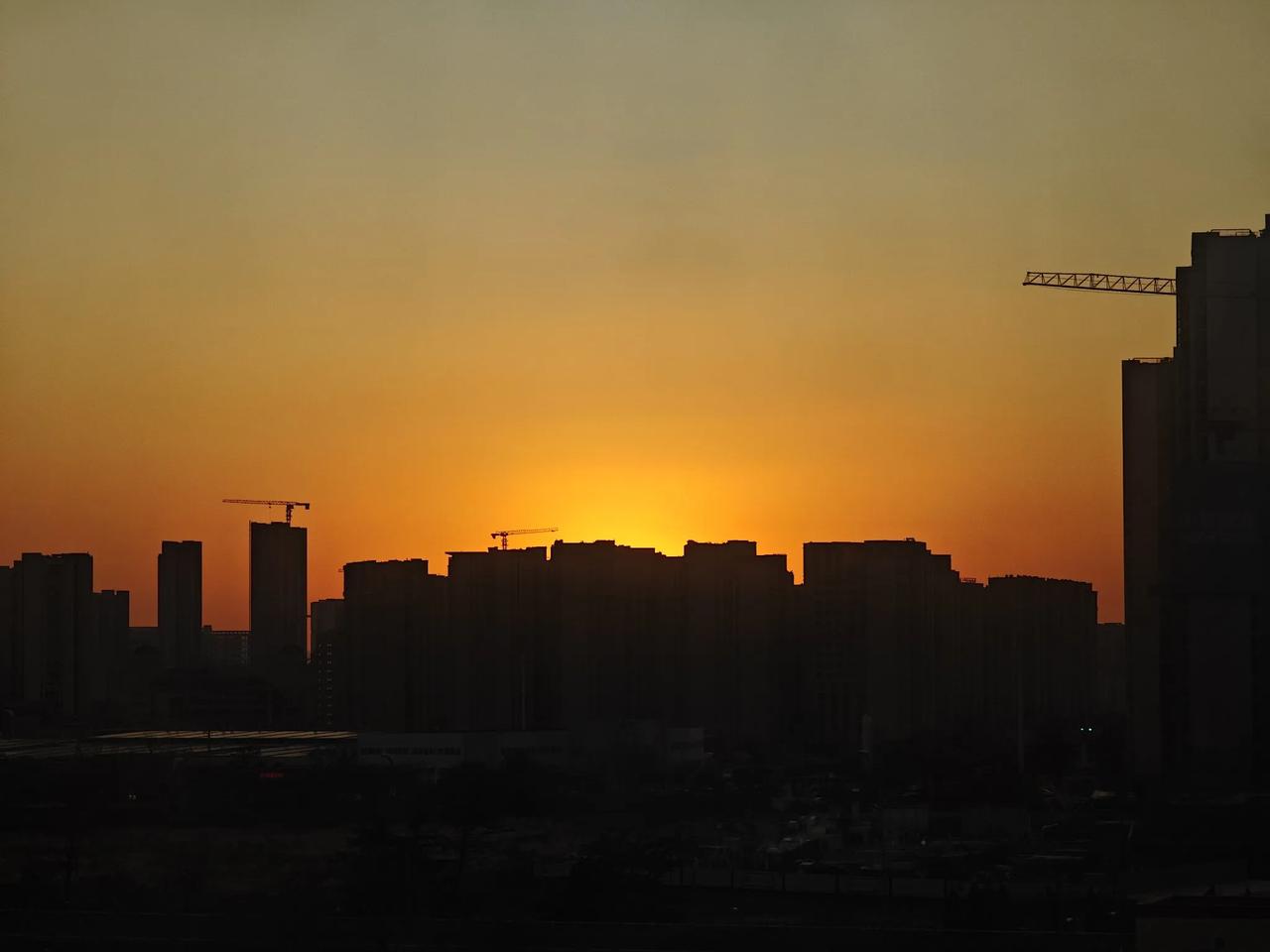 落日余晖映黄了半边天，余晖中城市的大楼和建筑工地塔架清晰可见，城市的一天就要结束