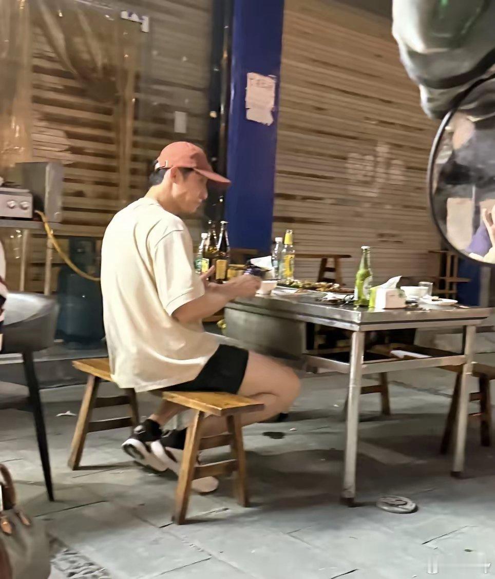 黄景瑜在乐山市一家路边摊吃烧烤，穿衣打扮很帅气，桌上放着好几瓶啤酒，路上人来人往