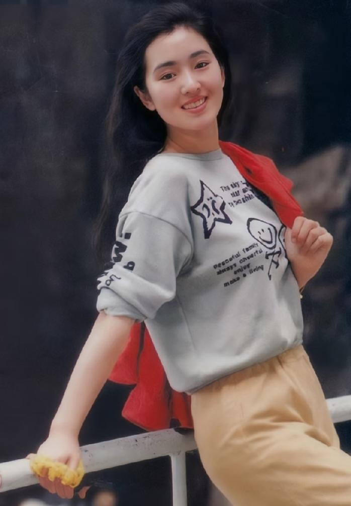 这张照片上的女子是年轻时的巩俐，她穿着灰色卫衣，眉眼弯弯，笑容灿烂，脸上满满的胶