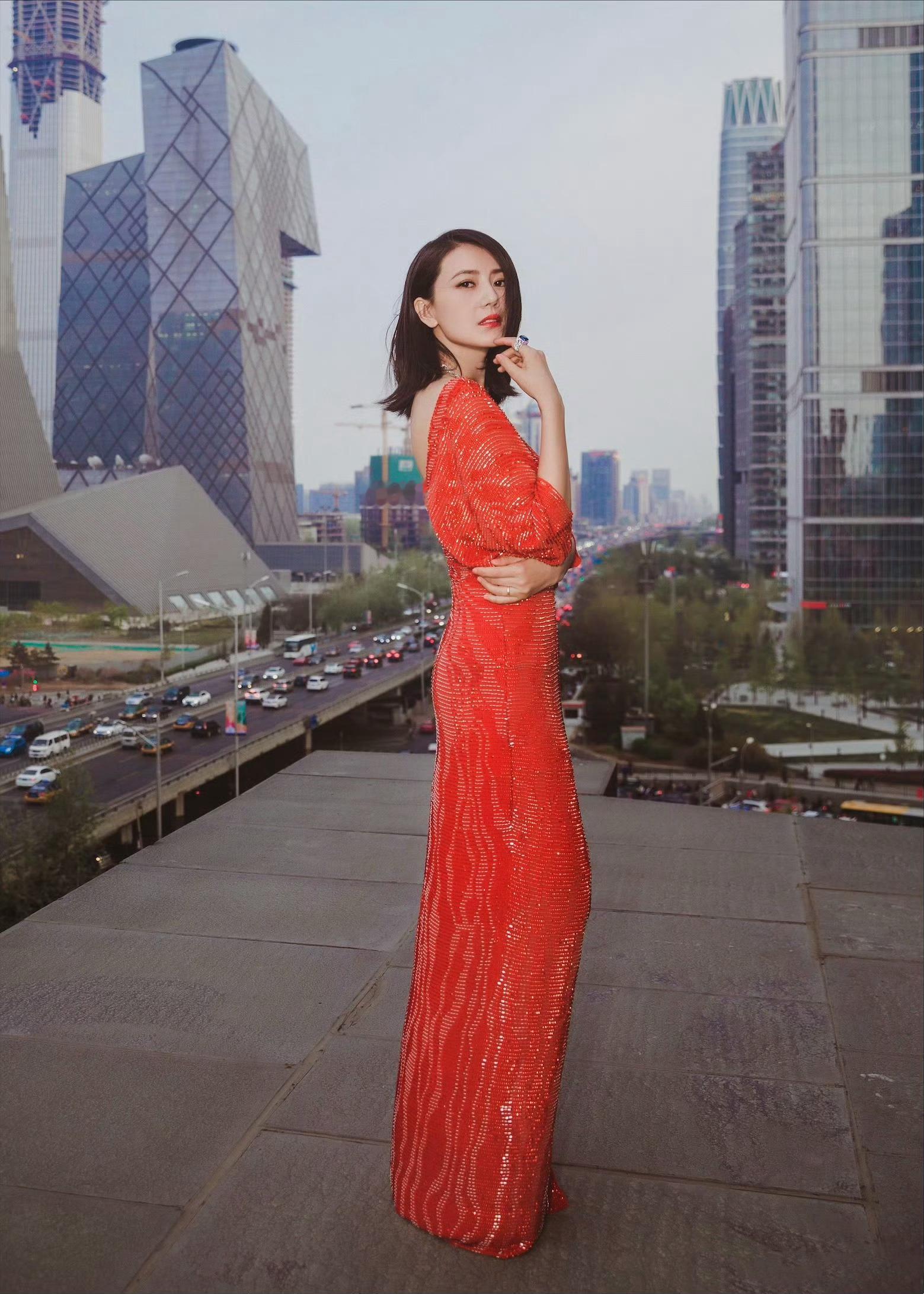 一袭红色亮片露背长裙，在城市建筑群背景下，笑容明媚，珠宝点缀更显优雅，时尚与都市