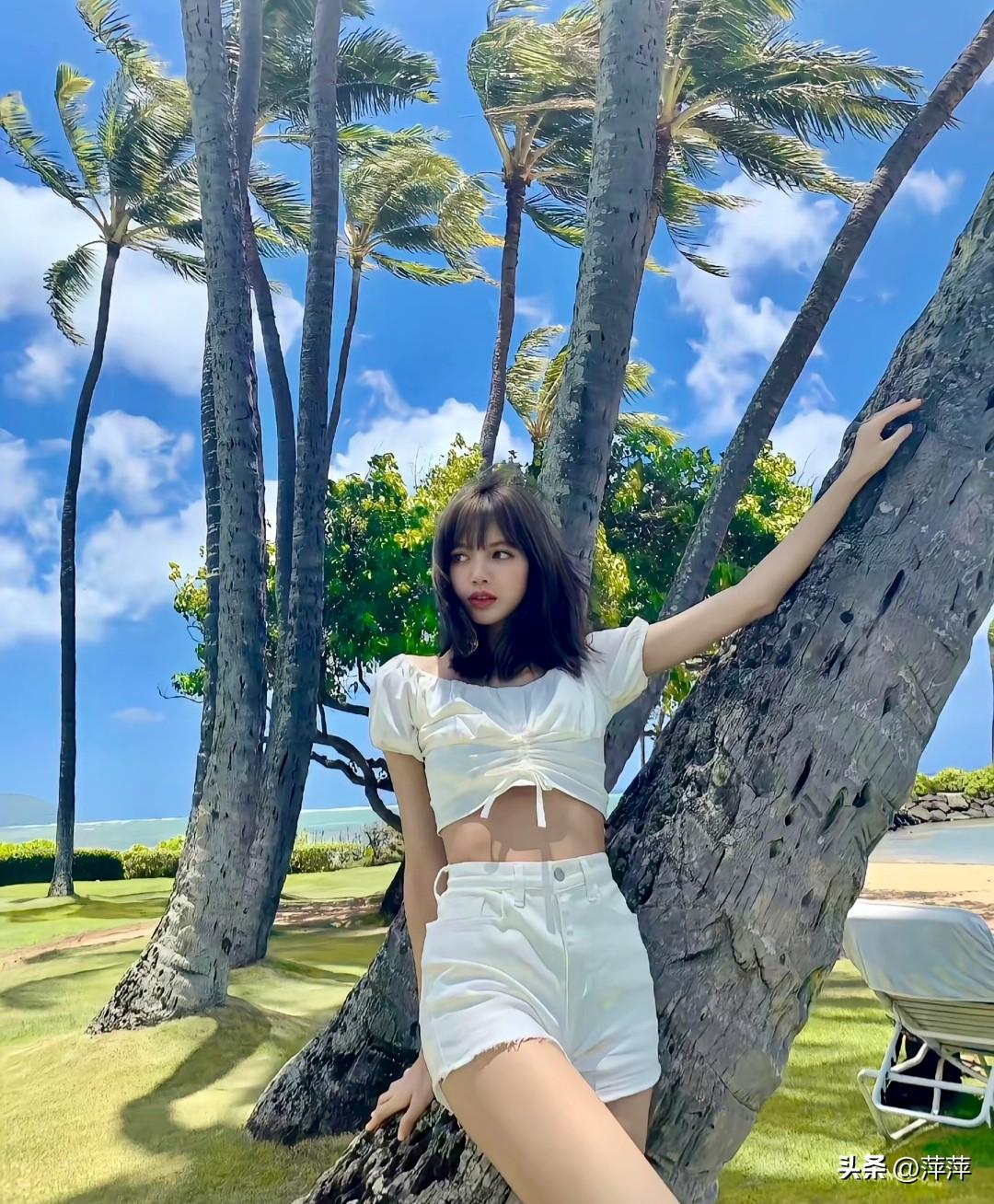 BLACKPINK成员Lisa身着纯白短款套装，倚靠椰树，在碧海蓝天间尽显灵动元