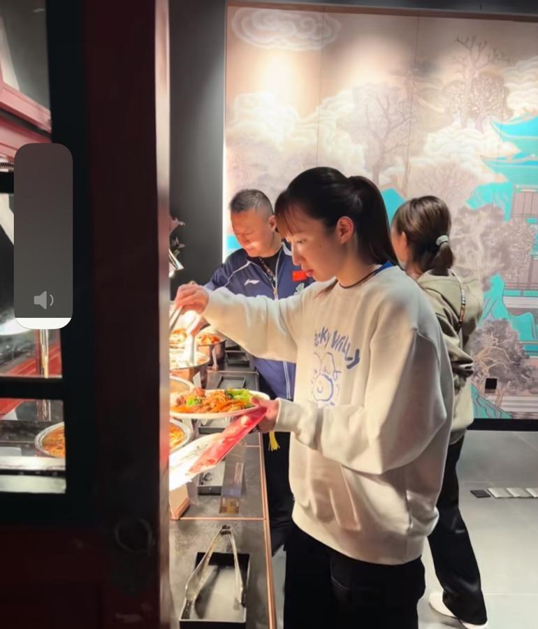 早田希娜端着盘子挤在首钢园自助餐台前，烤鸭夹得比谁都利索，旁边就是孙颖莎。这顿饭
