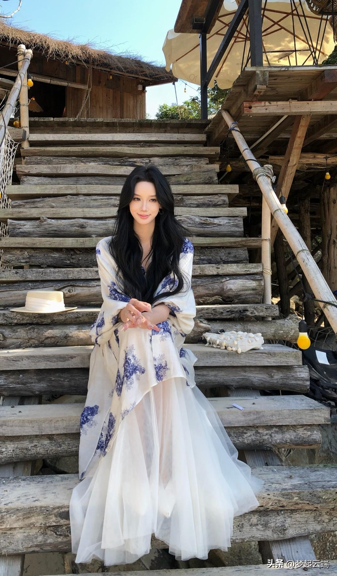 在古朴的木梯上，黑发美人穿着飘逸的蓝白长裙，静坐沉思。