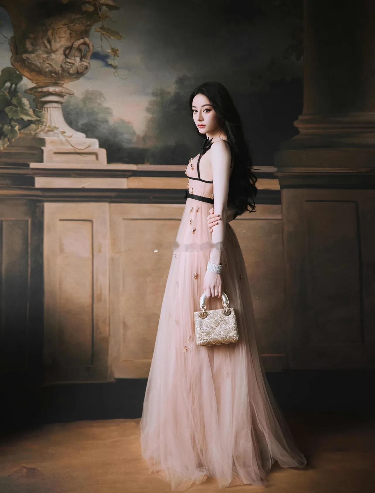 迪丽热巴微卷长发灵动飘逸，藕粉色网纱裙衬得肌肤胜雪，身姿窈窕火辣，甜辣气质扑面而