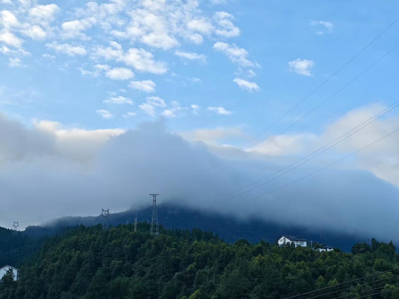 云雾漫过连绵的山脊，一半山体浸在朦胧雾气里，一半承接明媚日光。

层叠岩壁、幽深