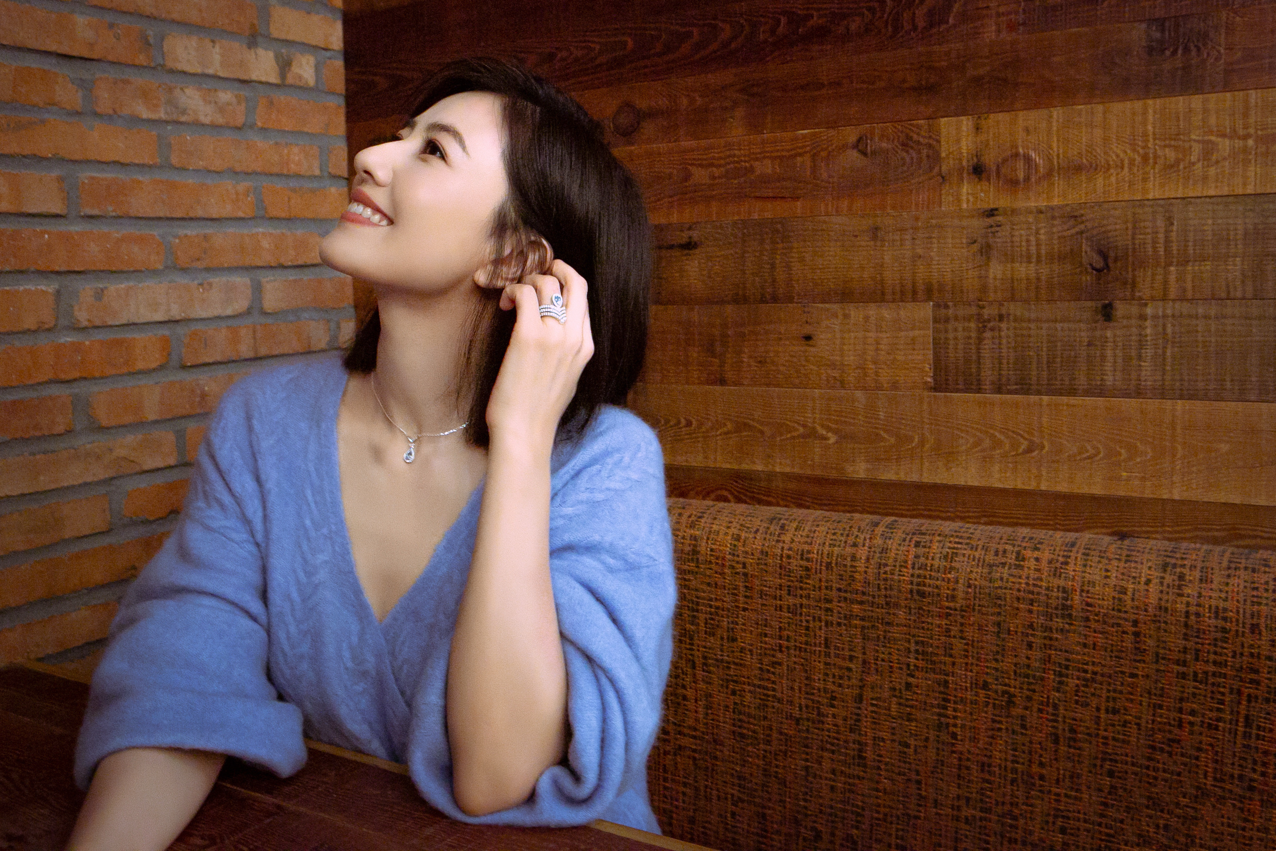 气质温婉又松弛，雾霾蓝的宽松毛衣衬得她温柔又慵懒，随意的姿态尽显从容。背景的红砖