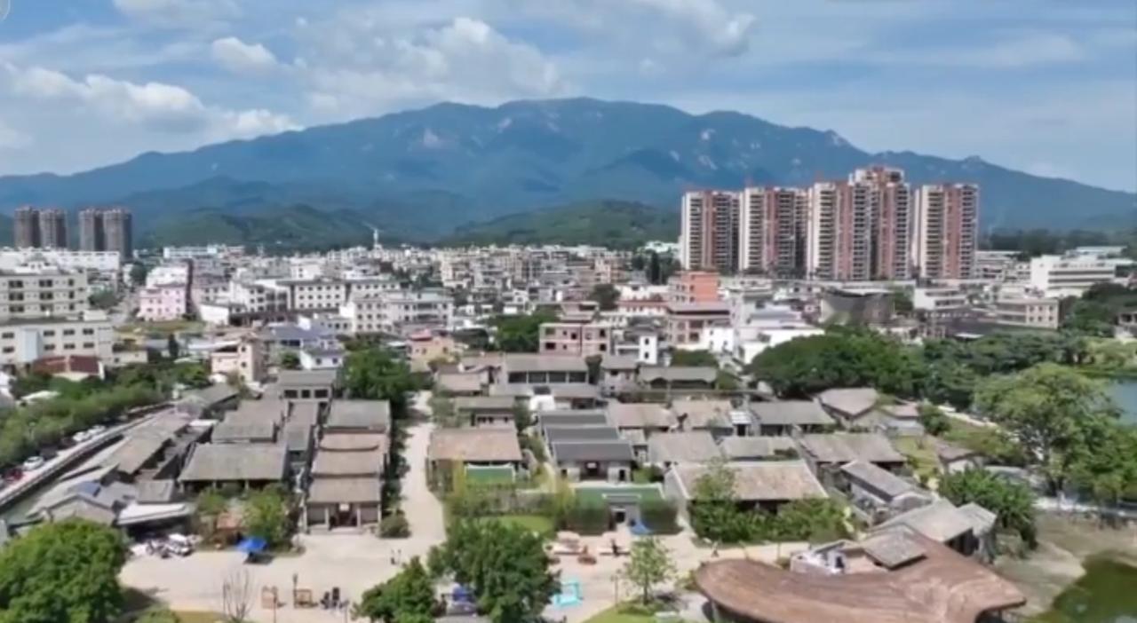 青山环抱的城镇里，老旧民居与现代高楼错落相依，远山如黛的背景勾勒出城乡融合的独特