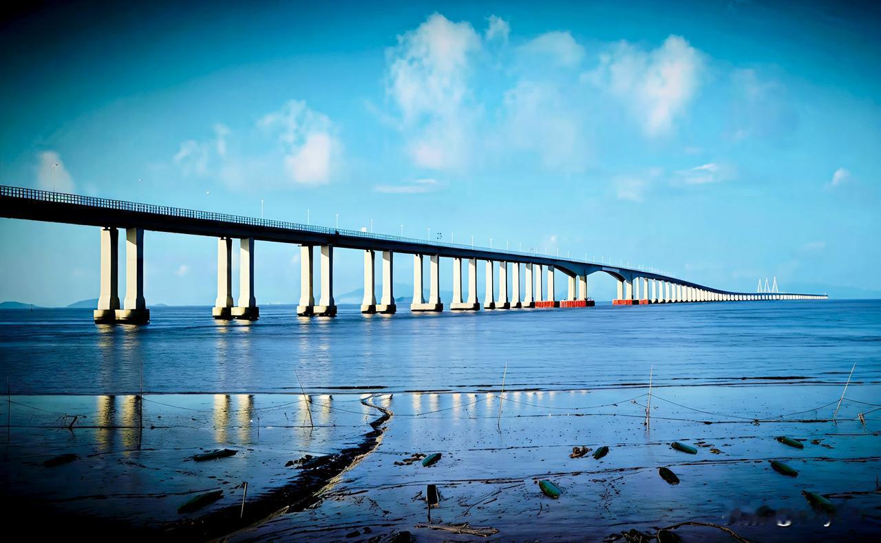 碧海之上，长桥卧波，舟岱大桥如银龙横亘海天。白墩列阵，红标映浪，三塔遥指云端。晴