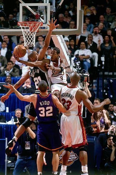 艾伦·艾弗森在全明星赛中绕过蒂姆·邓肯进行防守，而杰森·基德和阿隆佐·莫宁在一旁