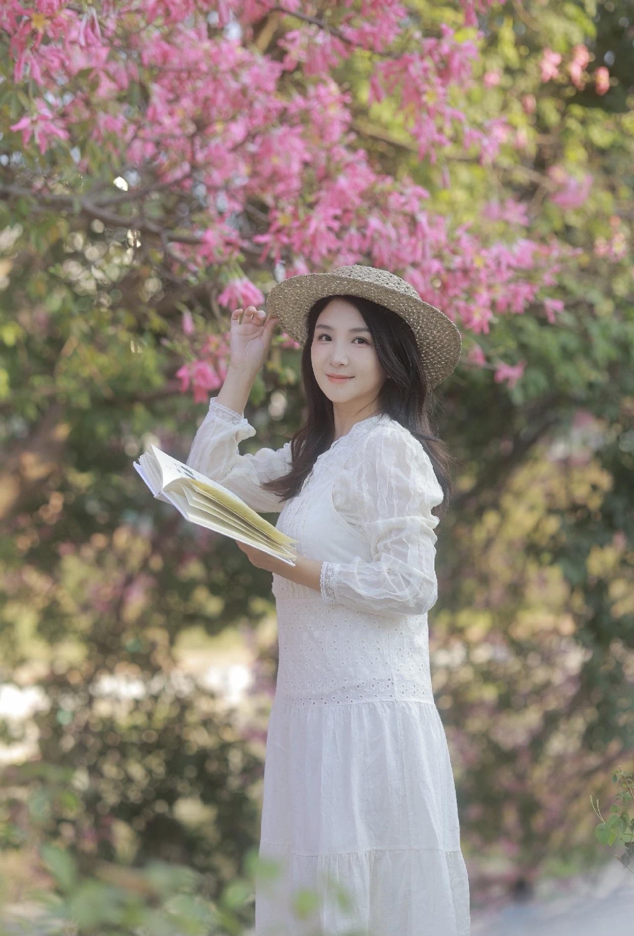 美少女美景分享粉色的花海中，一位优雅的少女手捧书本，沉浸在阅读的宁静时光里。