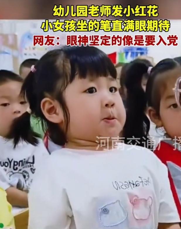 幼儿园课堂上老师正在分发小红花，一名小女孩端端正正坐得笔直，身体绷得紧紧的，满眼