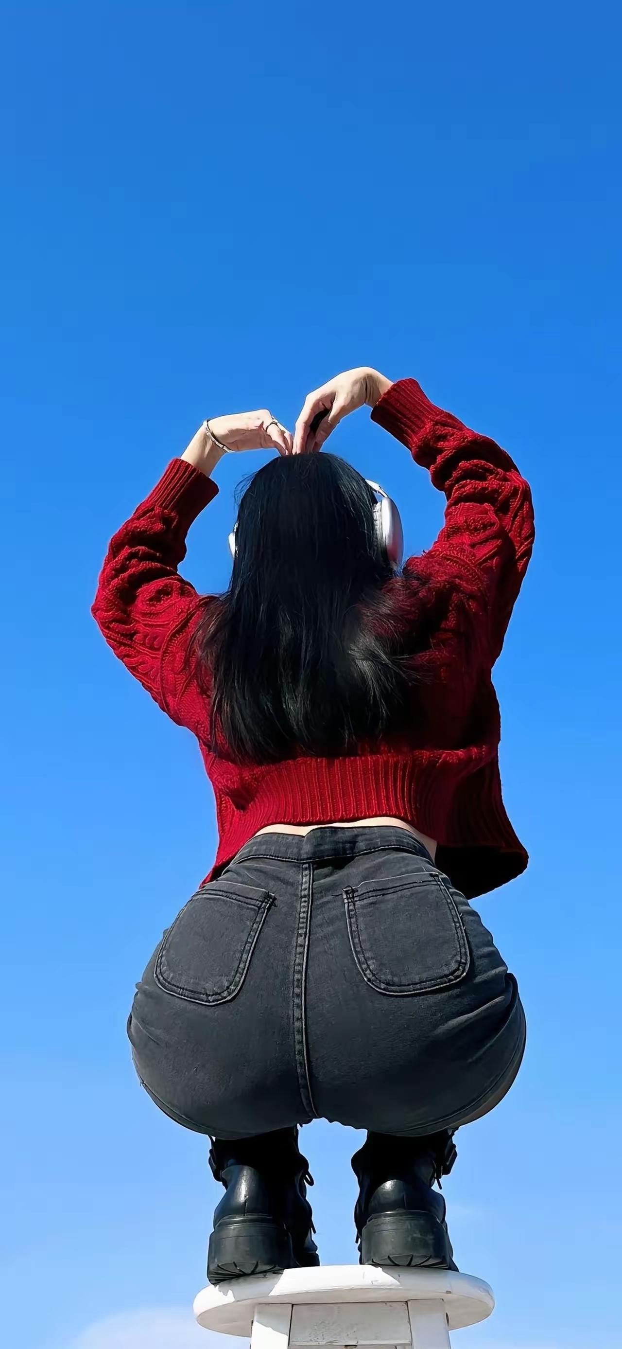 蓝天白云下，少女背对镜头，双手比心，红衣黑裤，青春洋溢。
